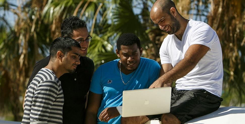 Four men looking at a laptop with palm trees in background