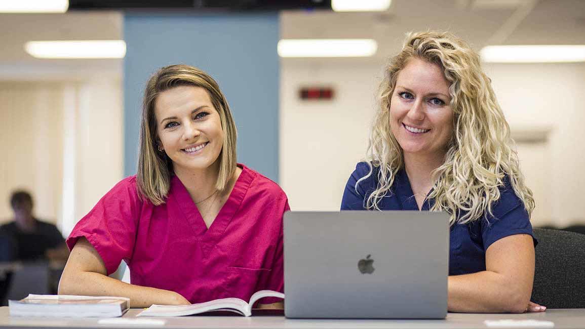 Two woman smiling for picture while studying